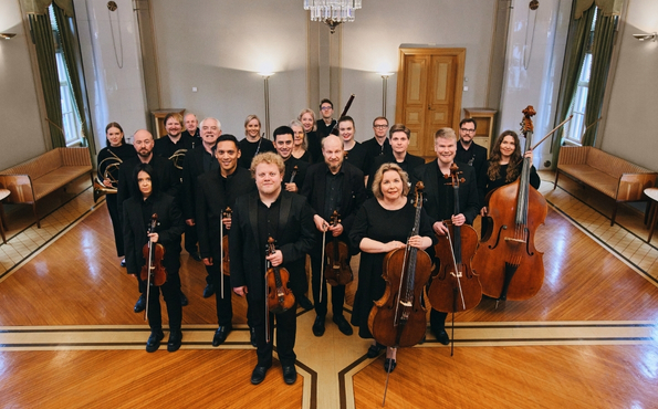 Kuvassa joukko orkesterimuusikoita soittimet kädessä mustiin konserttivaatteisiin pukeutuneina.
