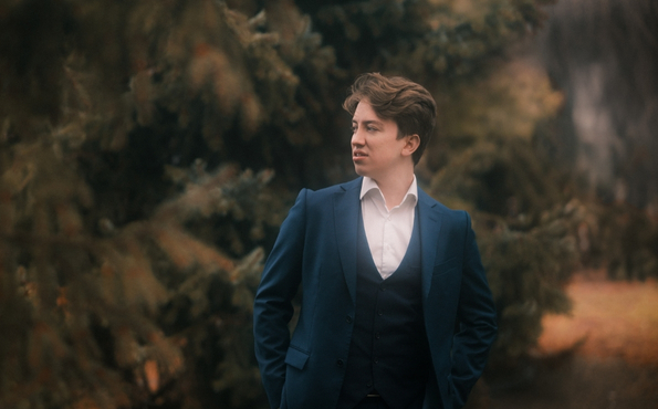 Nuori mies seisoo syksyisessä metsässä sinisessä puvussa. Hän kävelee kohti kameraa, katse on suunnattu vasemmalle.